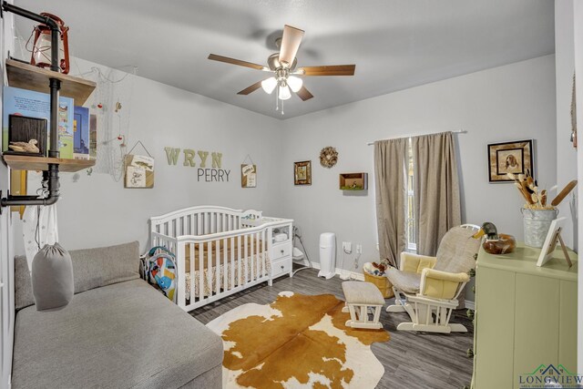 bedroom with hardwood / wood-style flooring, ceiling fan, and a nursery area