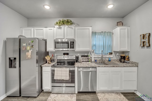 kitchen with appliances with stainless steel finishes, dark hardwood / wood-style floors, sink, white cabinets, and light stone countertops