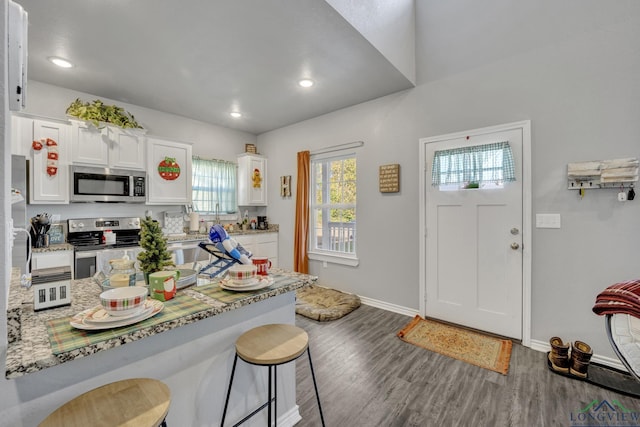 kitchen with a breakfast bar, white cabinets, hardwood / wood-style flooring, appliances with stainless steel finishes, and light stone counters