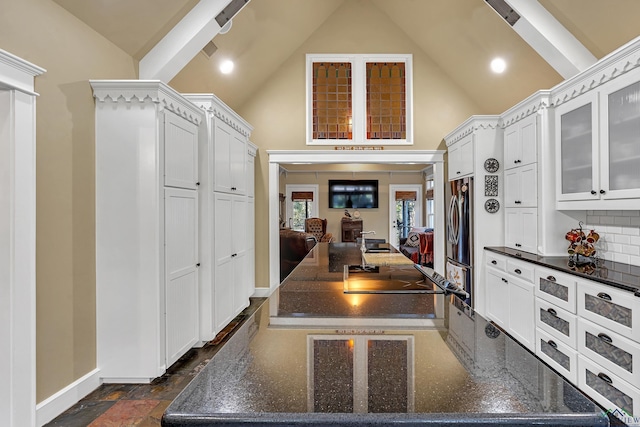 kitchen featuring stainless steel refrigerator, high vaulted ceiling, backsplash, dark stone countertops, and white cabinets