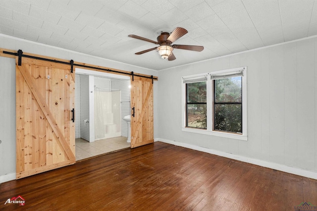 spare room with ceiling fan, wood-type flooring, crown molding, and a barn door