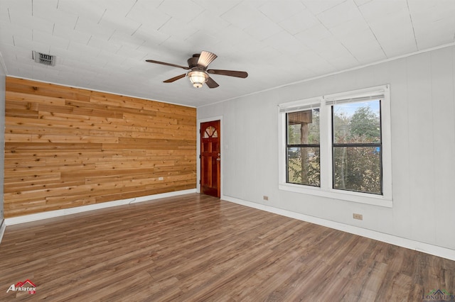 empty room with wood walls, ceiling fan, ornamental molding, and wood-type flooring