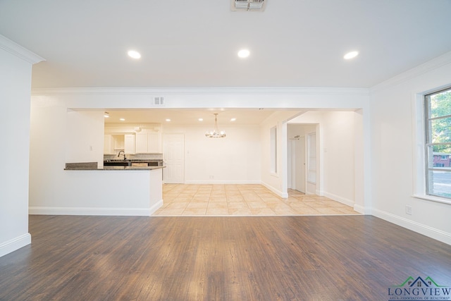 unfurnished living room featuring sink, light hardwood / wood-style floors, a notable chandelier, and ornamental molding