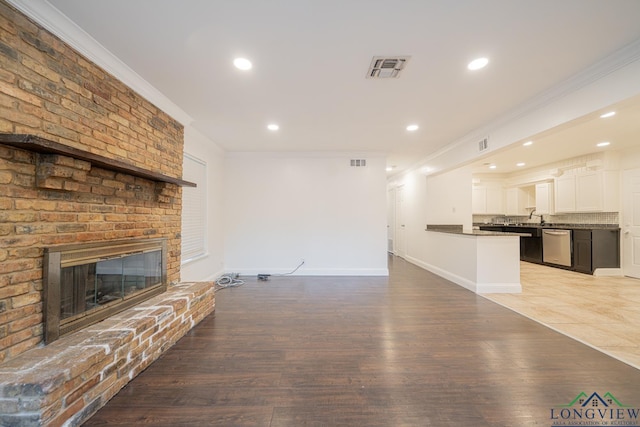 unfurnished living room with light wood-type flooring, a brick fireplace, ornamental molding, and sink