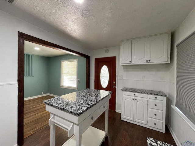 kitchen featuring white cabinets, dark wood finished floors, a textured ceiling, dark stone counters, and baseboards