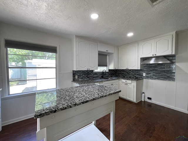 kitchen featuring dark stone countertops, a textured ceiling, a sink, backsplash, and white cabinetry