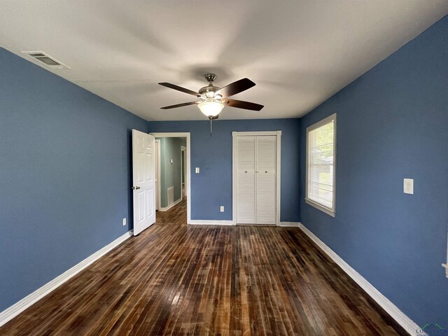 unfurnished bedroom featuring baseboards, dark wood finished floors, a closet, and a ceiling fan