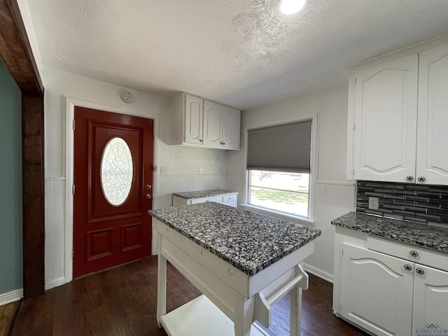kitchen with dark stone counters, a textured ceiling, white cabinets, dark wood finished floors, and decorative backsplash