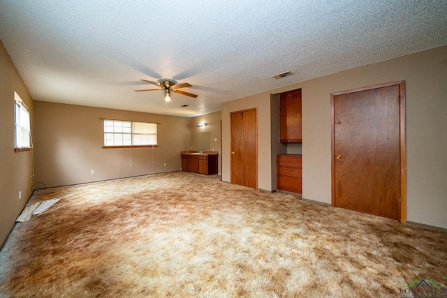 unfurnished living room featuring light carpet, visible vents, a textured ceiling, and a ceiling fan