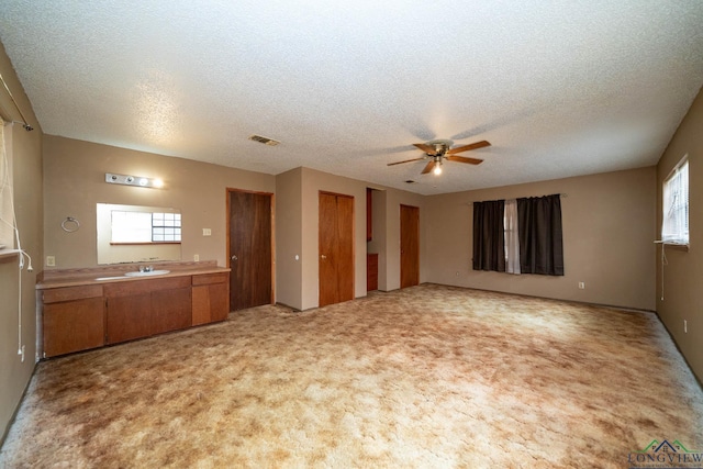 unfurnished living room with light colored carpet, visible vents, ceiling fan, a textured ceiling, and a sink