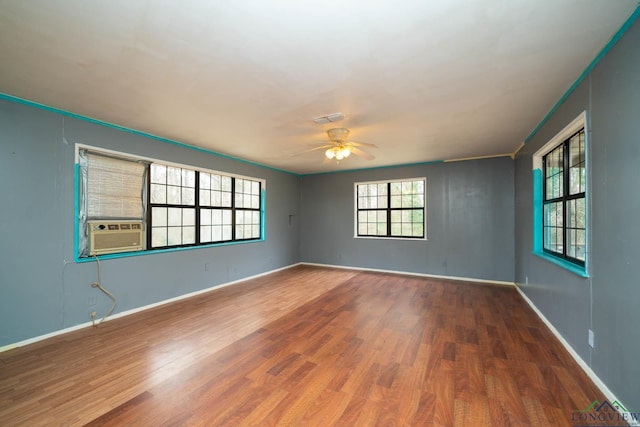 unfurnished room featuring cooling unit, visible vents, baseboards, and wood finished floors