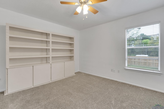 empty room with built in shelves, light carpet, and ceiling fan