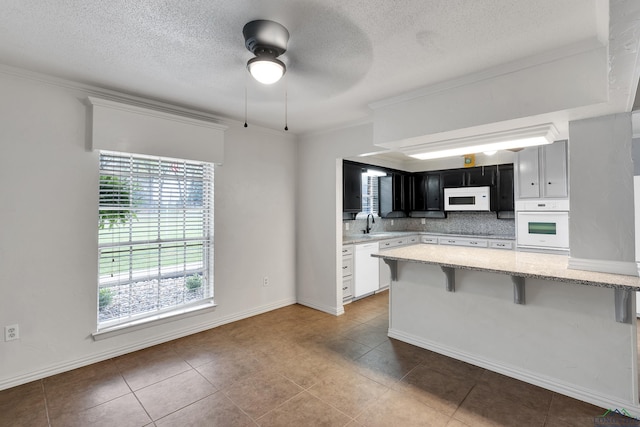 kitchen featuring a breakfast bar, white appliances, backsplash, ceiling fan, and kitchen peninsula