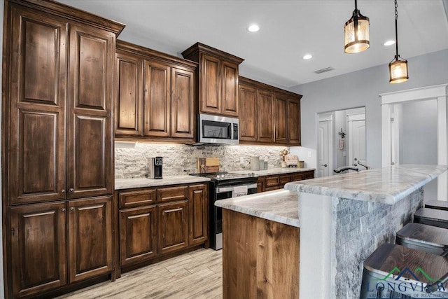 kitchen with a kitchen breakfast bar, hanging light fixtures, an island with sink, appliances with stainless steel finishes, and light stone counters