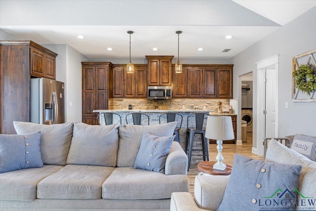 living room featuring washer / clothes dryer, light hardwood / wood-style floors, and lofted ceiling