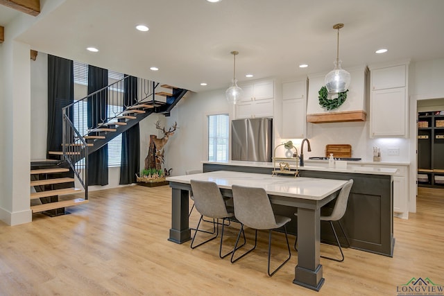 kitchen featuring white cabinetry, stainless steel fridge, a center island with sink, and decorative light fixtures