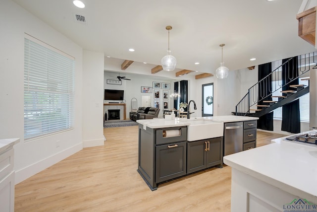 kitchen with gray cabinetry, an island with sink, hanging light fixtures, and beamed ceiling