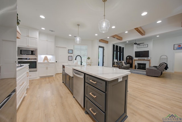 kitchen with appliances with stainless steel finishes, light wood-type flooring, decorative light fixtures, white cabinetry, and an island with sink