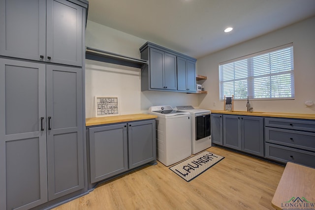 laundry room featuring cabinets, light hardwood / wood-style floors, washing machine and clothes dryer, and sink