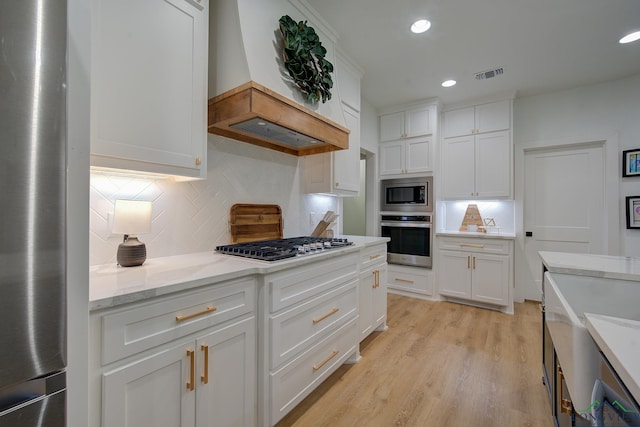 kitchen with white cabinets, custom range hood, backsplash, and appliances with stainless steel finishes