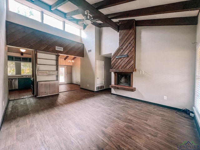 unfurnished living room with dark wood-type flooring, a high ceiling, ceiling fan, beam ceiling, and a large fireplace