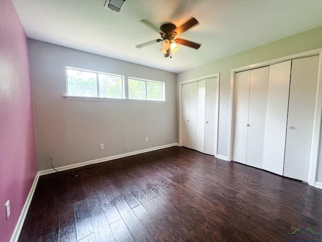 unfurnished bedroom with two closets, ceiling fan, and dark wood-type flooring