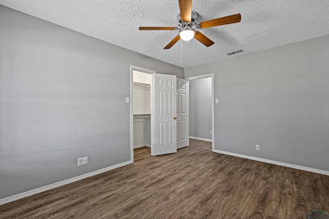 unfurnished bedroom with a spacious closet, a textured ceiling, dark wood-type flooring, a closet, and ceiling fan