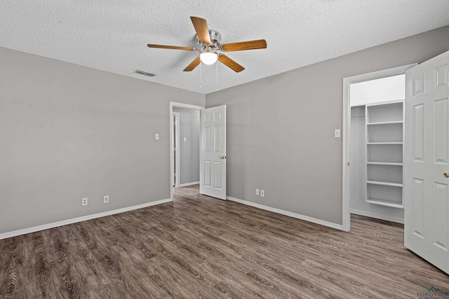 unfurnished bedroom featuring a textured ceiling, ceiling fan, a spacious closet, and dark wood-type flooring