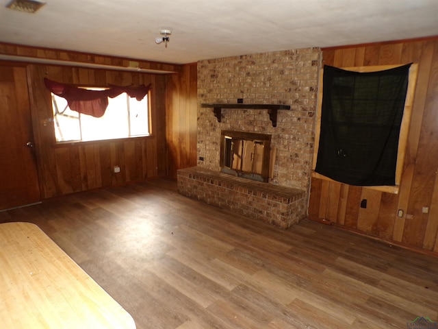 unfurnished living room featuring a brick fireplace, wooden walls, and hardwood / wood-style flooring