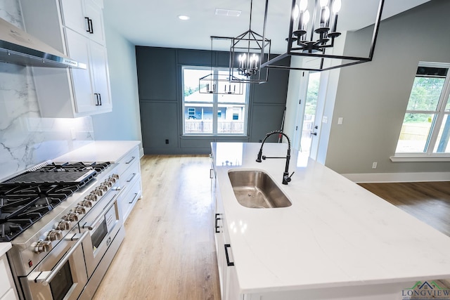 kitchen with white cabinetry, hanging light fixtures, an island with sink, double oven range, and exhaust hood