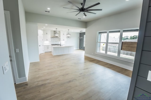 unfurnished living room with ceiling fan with notable chandelier, light hardwood / wood-style flooring, and sink