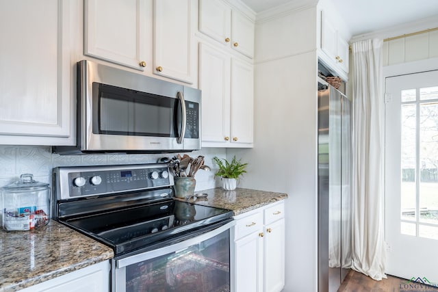 kitchen featuring white cabinets, appliances with stainless steel finishes, ornamental molding, and dark stone countertops