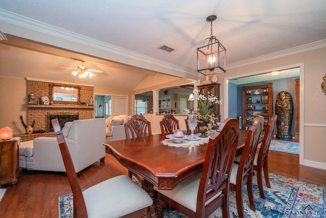 dining room with a brick fireplace, crown molding, dark wood-type flooring, and ceiling fan