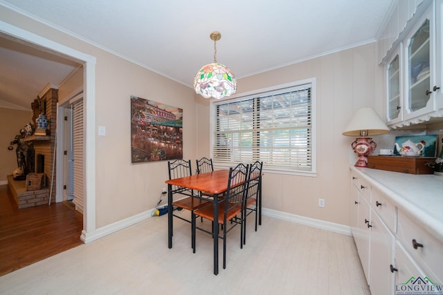 dining room with crown molding, a brick fireplace, and light hardwood / wood-style flooring