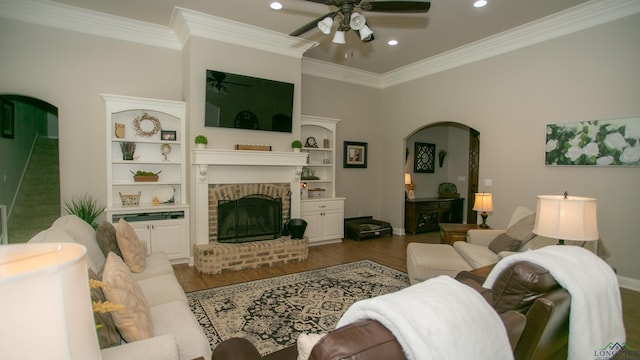 living room with a brick fireplace, ceiling fan, crown molding, hardwood / wood-style flooring, and built in features