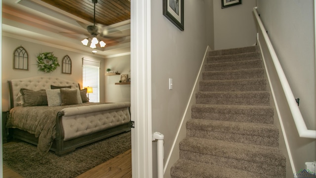 stairway featuring hardwood / wood-style floors, ceiling fan, crown molding, and a tray ceiling