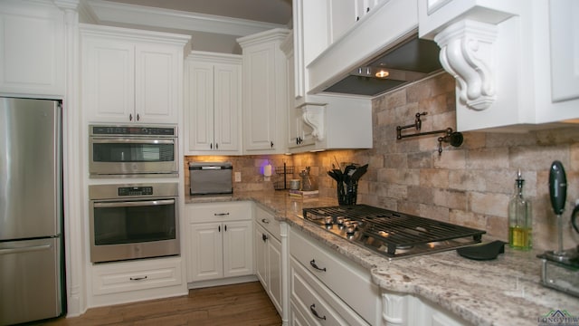 kitchen with backsplash, light stone countertops, white cabinetry, and stainless steel appliances