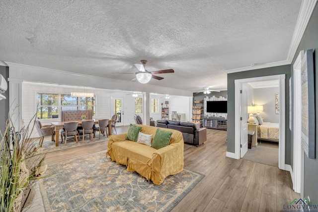 living area with a textured ceiling, crown molding, baseboards, ceiling fan, and light wood-type flooring