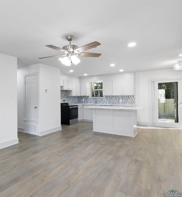 kitchen with light wood-type flooring, tasteful backsplash, ceiling fan, white cabinets, and stainless steel range with electric cooktop