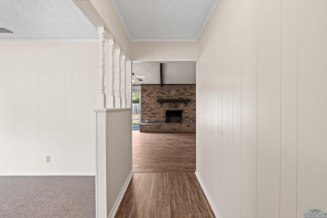 hall featuring a textured ceiling, dark wood-type flooring, visible vents, ornamental molding, and decorative columns