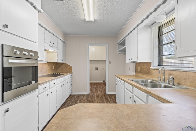 kitchen featuring oven, black electric stovetop, light countertops, white cabinetry, and a sink