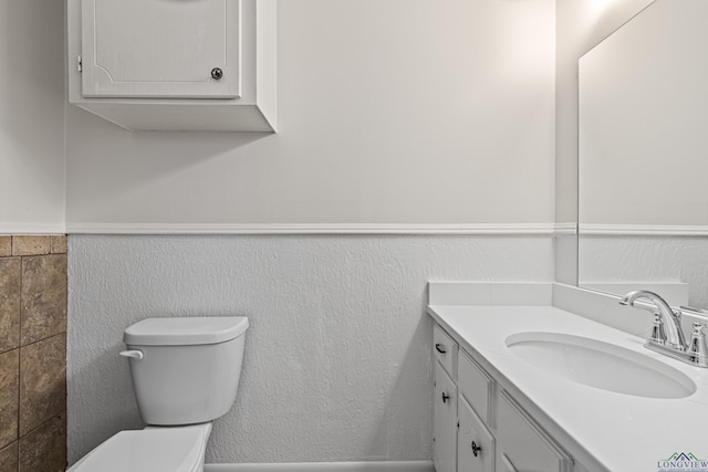 half bath with wainscoting, vanity, and toilet