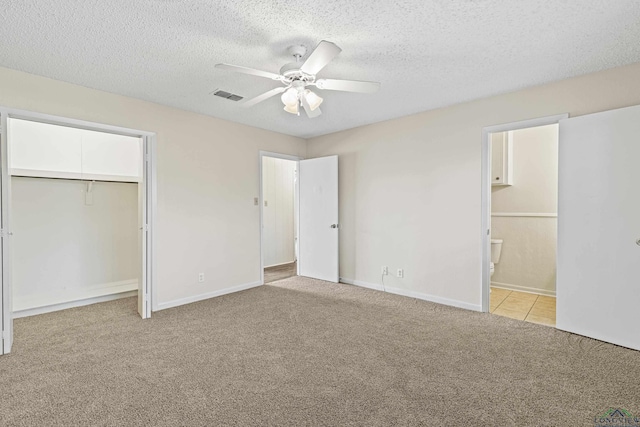 unfurnished bedroom featuring light colored carpet, visible vents, connected bathroom, a textured ceiling, and baseboards