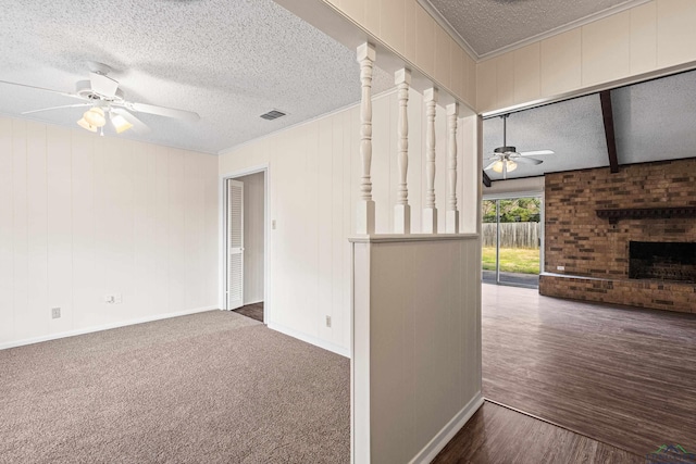 spare room featuring a textured ceiling, visible vents, a ceiling fan, a brick fireplace, and beam ceiling