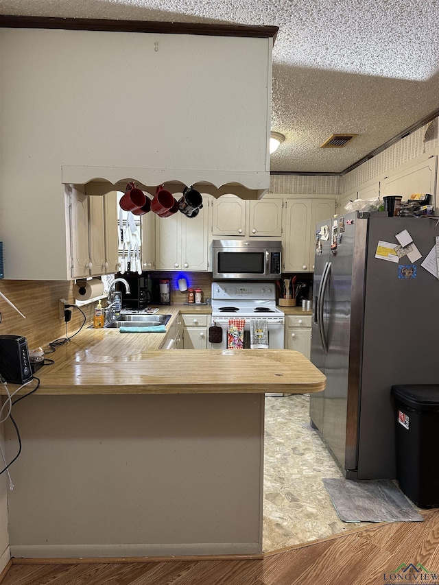 18335 Fm 1716 E, Tatum, TX 75691 - kitchen with sink, a textured ceiling, light wood-type flooring, kitchen peninsula, and stainless steel appliances
