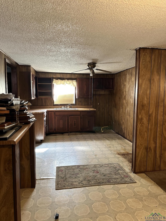 kitchen featuring wooden walls, dark brown cabinets, ceiling fan, and sink