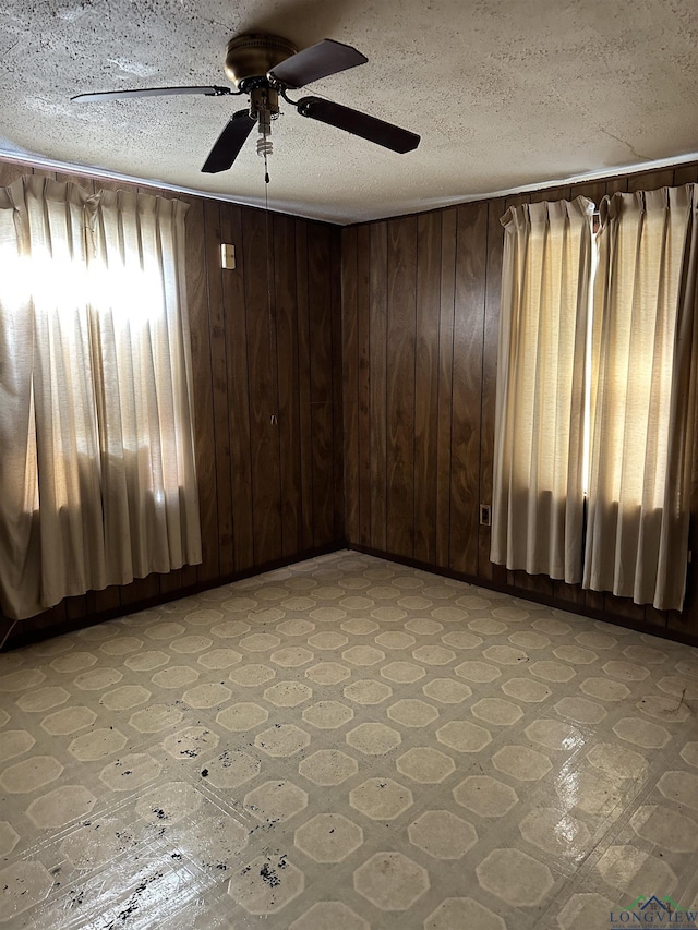 spare room with ceiling fan, wood walls, and a textured ceiling