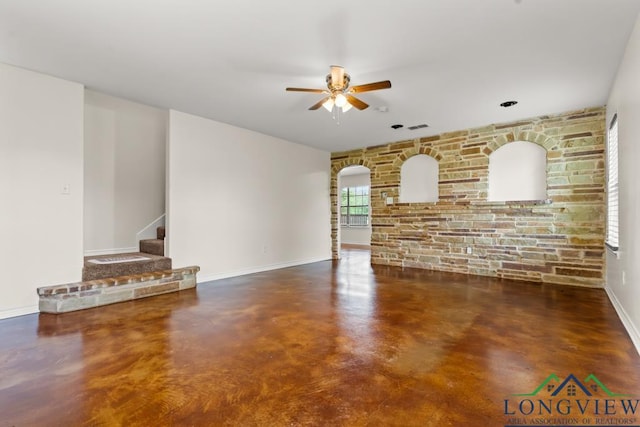 unfurnished living room featuring a ceiling fan, arched walkways, concrete flooring, baseboards, and stairs