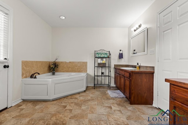 full bath with baseboards, stone finish floor, a garden tub, and vanity