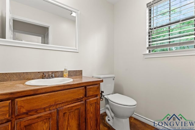 half bath with toilet, baseboards, and vanity